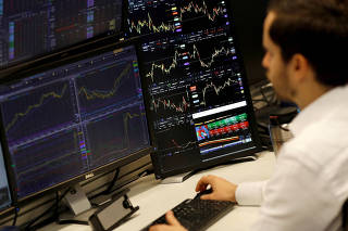 FILE PHOTO: A financial trader works at their desk at CMC Markets in the City of London