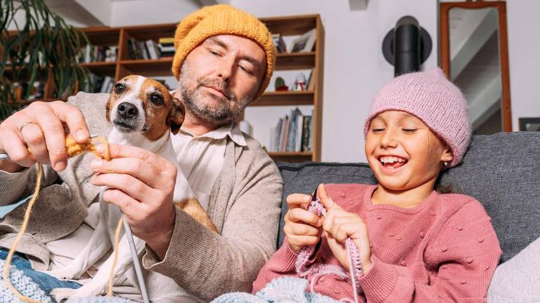 Pai e filha tricotando, com um cachorrinho no colo