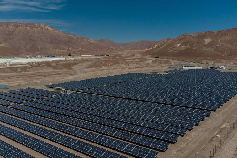 Vista aérea planta fotovoltaica, com diversos painéis solares em meio a paisagem desértica e montanhosa