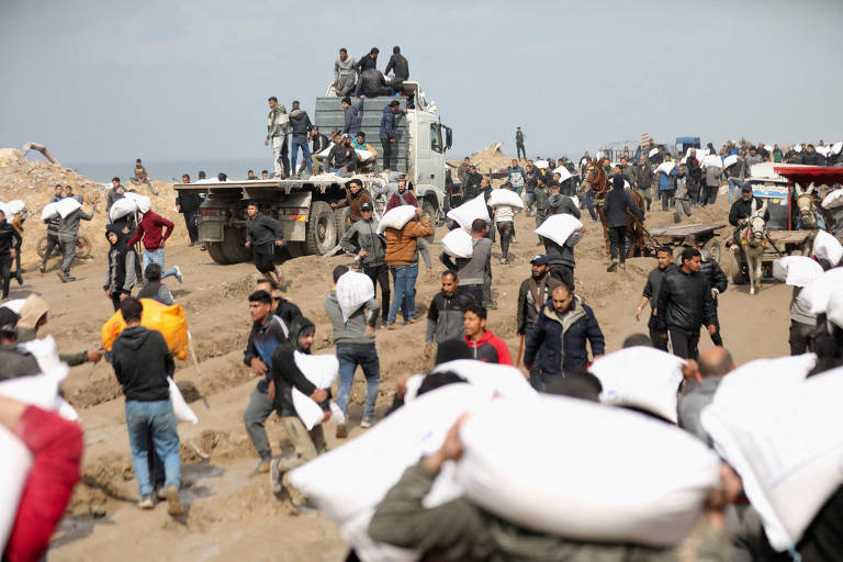 Palestinos carregam sacos de farinha que pegaram de um caminhão de ajuda perto de um posto de controle israelense, na Cidade de Gaza