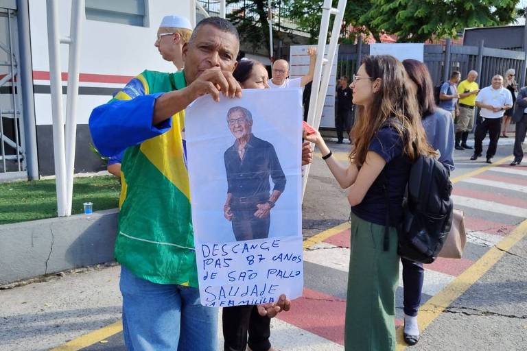 Homem de roupa  verde e amarela segura cartaz com a foto de Abilio Diniz