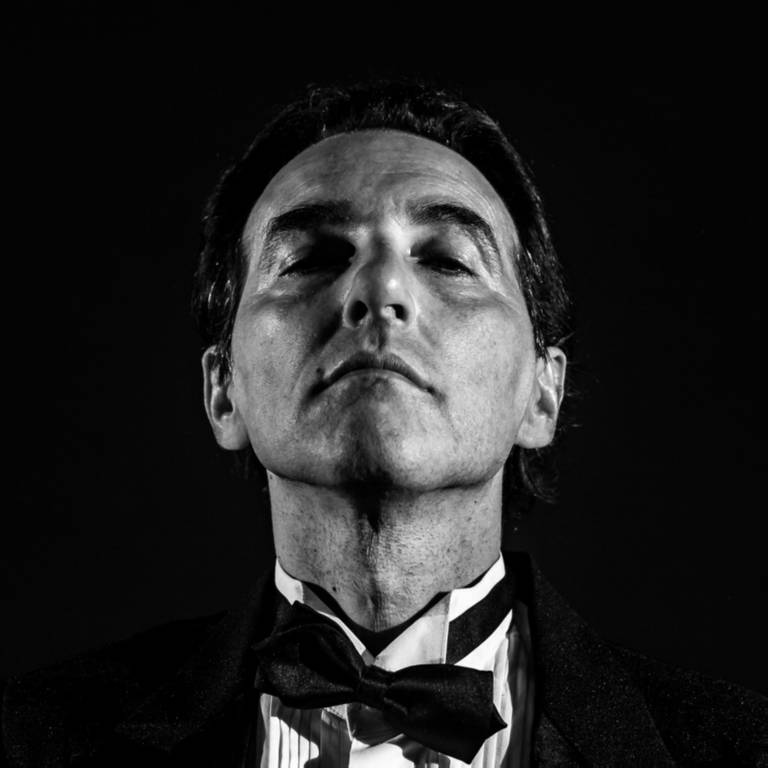 Em foto preto e branco, o  cantor, compositor e instrumentista Márcio de Camillo posa para a câmera de gravata borboleta