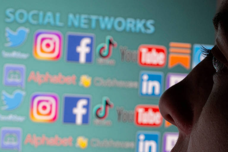 Pessoa observa tela com símbolos de redes sociais como Facebook, Instagram, TikTok, X, YouTube, LinkedIn e WhatsApp