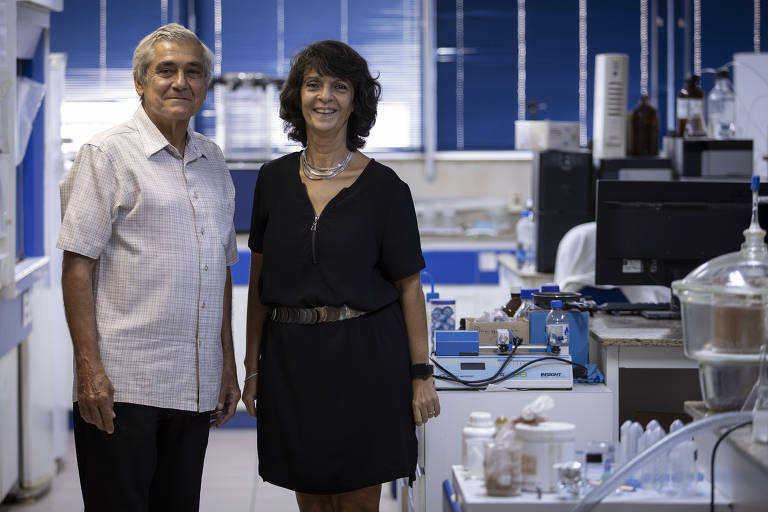 A imagem mostra o casal em um laboratório de química da UFRJ, com equipamentos científicos. O espaço tem paredes azuis. 