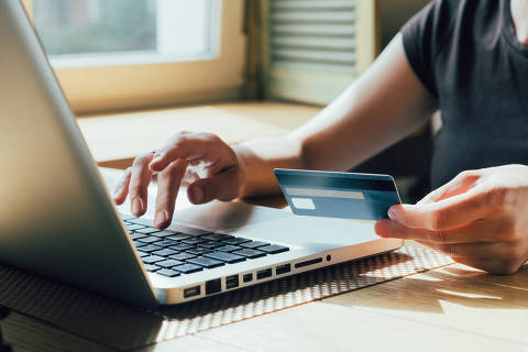 Garota faz uma compra na internet no computador com cartão de crédito. Compra online