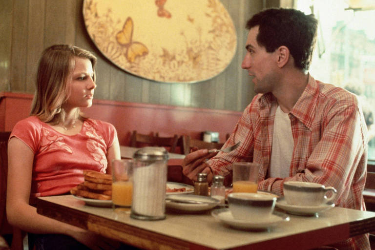 Uma adolescente e um homem jovem conversam à mesa de uma lanchonete
