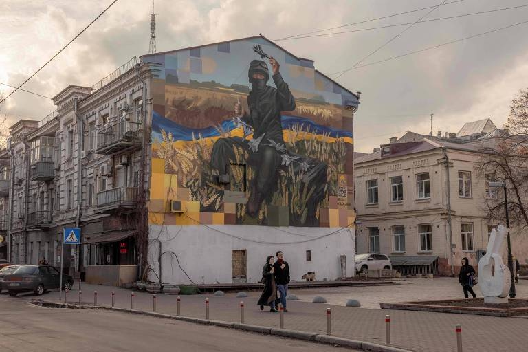 Moradores caminham perto de mural de soldado no bairro de Podil, na capital ucraniana, Kiev