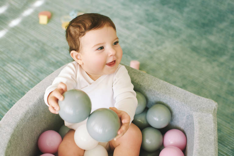 Imagem de um bebê branco brincando com bolas de plástico coloridas
