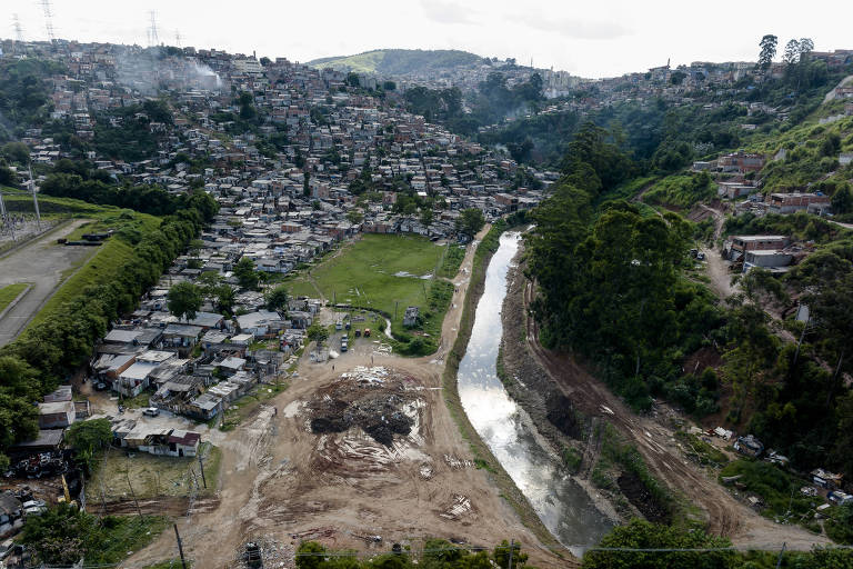 Imagem aérea mostra rio cortado por avenida e, nas margens, uma favela