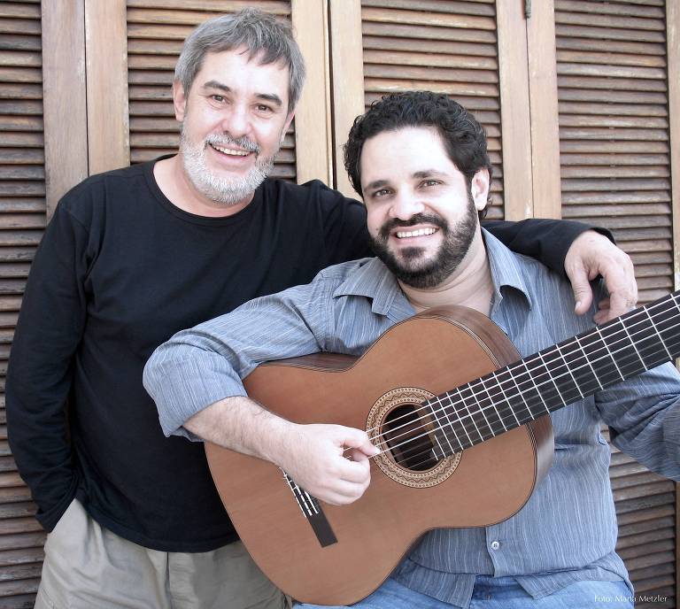 Em foto colorida, Marco Pereira e Rogério Caetano posam para a câmera sorrindo  