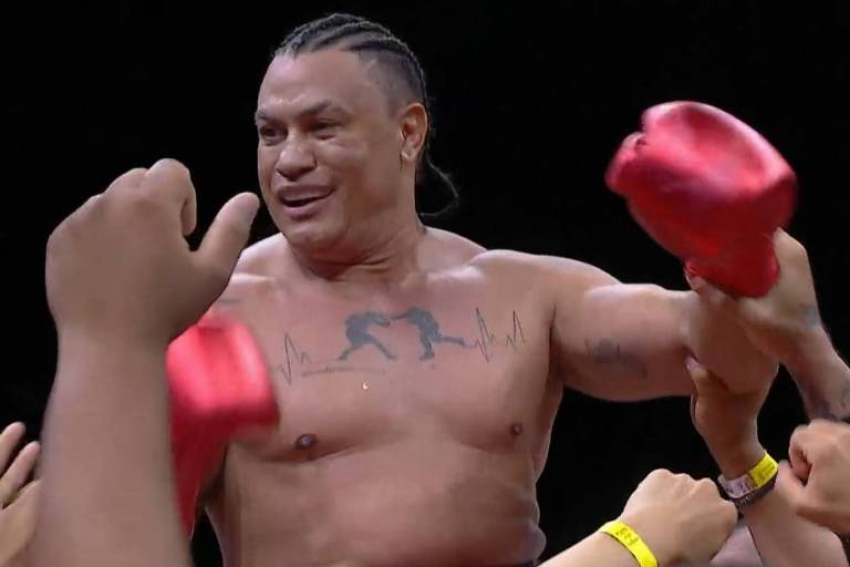 A imagem mostra o lutador Popó sorrindo e usando luvas de boxe