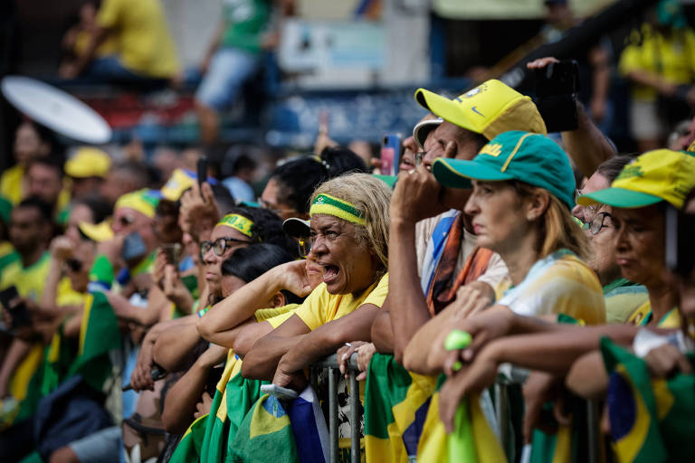 Ato na avenida Paulista em defesa de Bolsonaro; numa grade, pessoas vestidas com camisetas e acessórios nas cores verde e amarelo de aglomeram