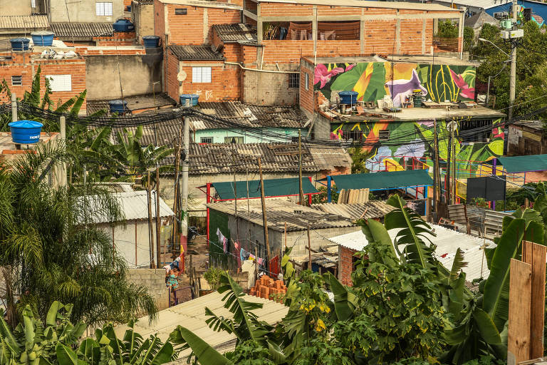 Imagem mostra casas feitas de tijolos vermelhos e algumas paredes pintadas com murais e copas de folhas de bananeiras