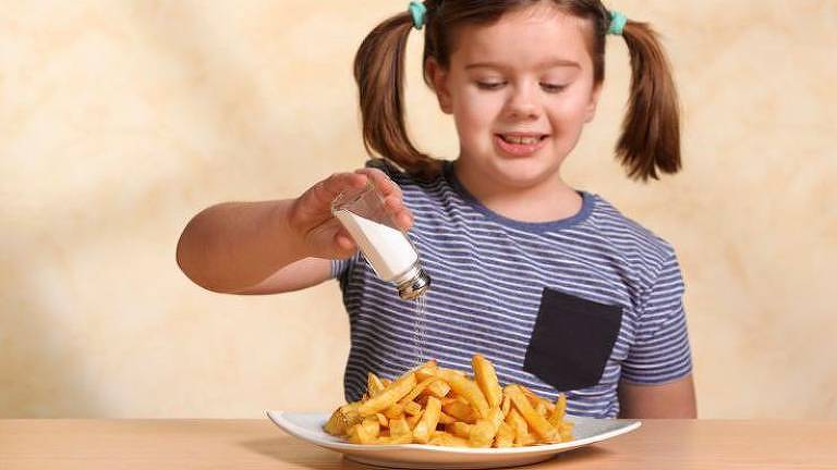 Menina colocando sal num prato com batatas fritas