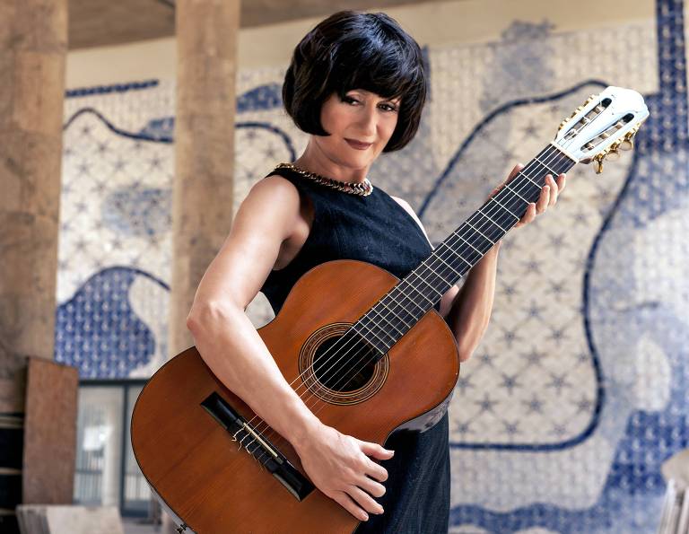 Em foto colorida, a atriz Zezé Polessa posa para a câmera com um violão na mão
