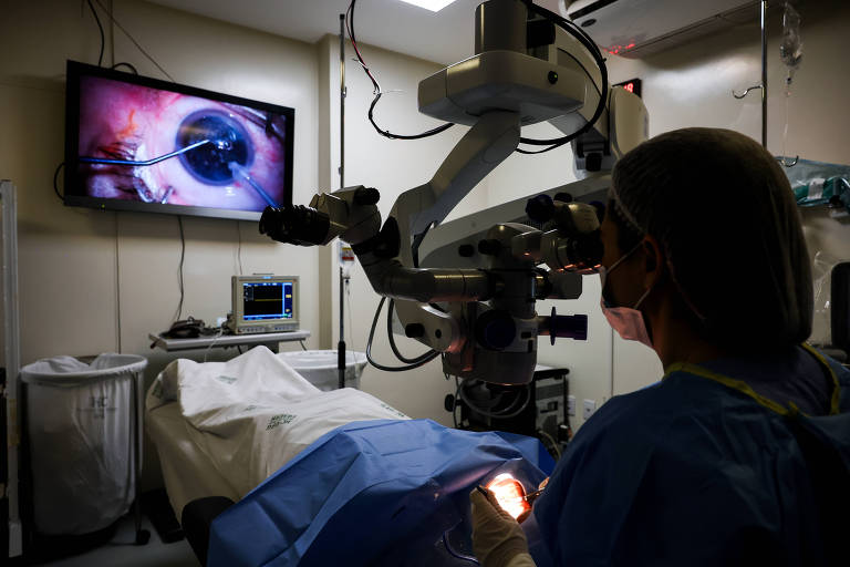 Oftalmologista realiza cirurgia de catarata em paciente, tem um aparelho cirúrgico e uma televisão com foco no olho operado.