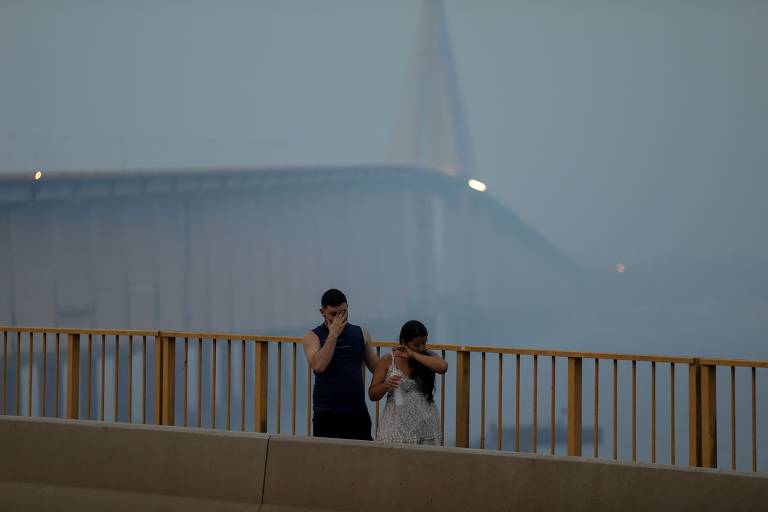 Um casal caminha em ponte de Manaus sob a névoa de fumaça dos incêndios na floresta amazônica que invadiu a cidade em 13 de outubro de 2023