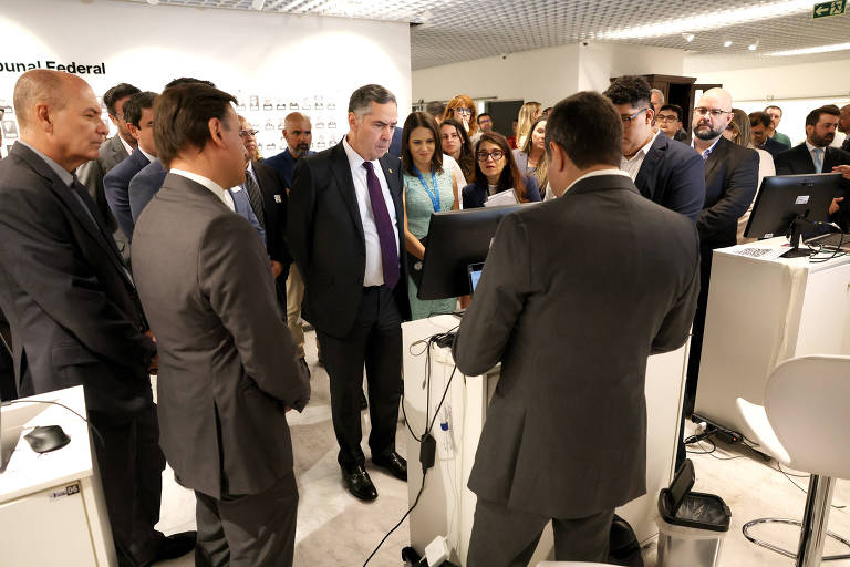 Vários pessoas em trajes formais. No centro, Luís Roberto Barroso olha para um monitor de computador.