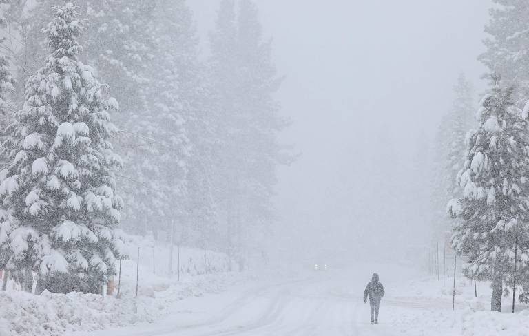 Pessoa caminha enquanto a neve cai ao norte do Lago Tahoe, nas montanhas de Sierra Nevada (Califórnia), durante tempestade de inverno
