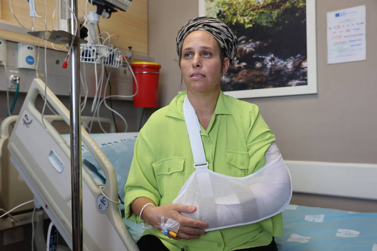 Mulher branca com roupa verde em hospital com braço enfaxiado