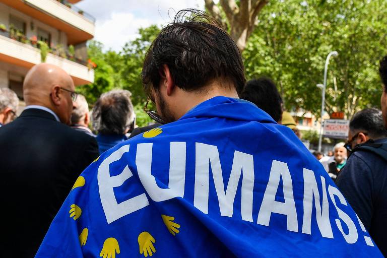 Homem usa bandeira nas costas com o escrito: EUMANS!