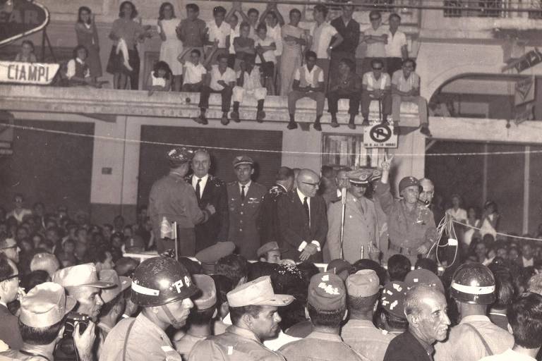 O general Olympio Mourão Filho (com cachimbo) e o governador de Minas Gerais, Magalhães Pinto (de terno, gravata e óculos), em palanque durante a festa de retorno das tropas a Juiz de Fora (MG) após o vitorioso golpe de 1964