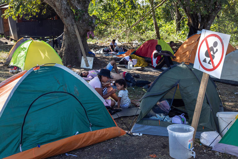 Imigrantes abrigados na Estação de Recepção Migratória de Lajas Blancas, na Comarca Emberá; à direita, placa indica que é proibido fazer necessidades no local