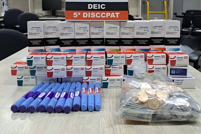 caixas de remédios em uma mesa com o símbolo da polícia no fundo