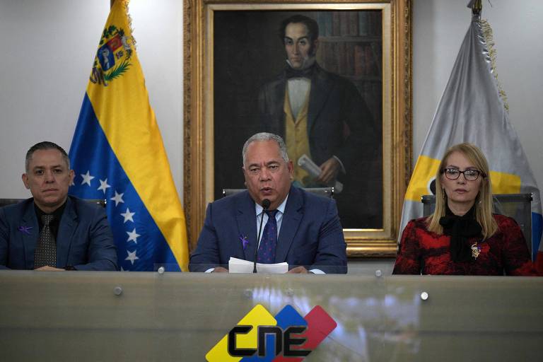 Sentado em uma mesa com o logo da CNE, Elvis lê um papel ao microfone, flanqueado por dois funcionários do órgão. Atrás dele se vê um quadro de Simon Bolívar e uma bandeira da Venezuela.