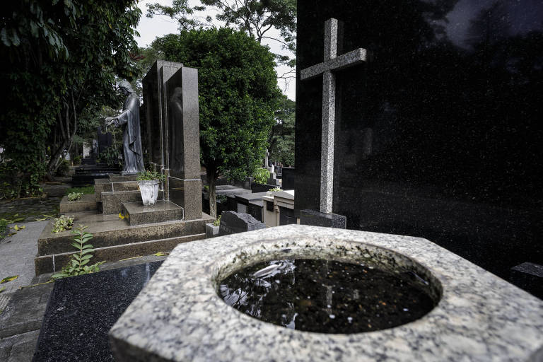 Fotografia de um vaso com água parada em frente a um túmulo