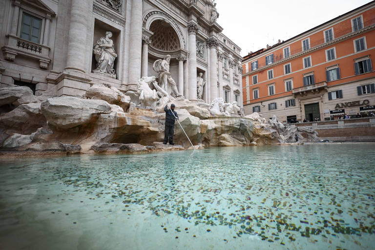 Daniele Rapiti, funcionária da concessionária ACEA, usa uma vassoura para juntar moedas na Fonte de Trevi, em Roma, Itália, em 19 de fevereiro de 2024