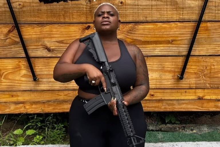 Em foto colorida,mulher toda vestida de preto posa segurando um fuzil