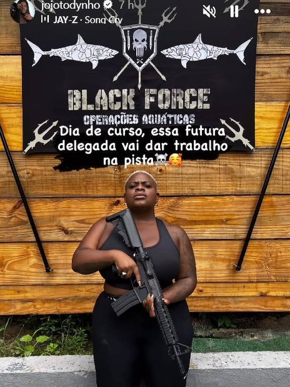 Em foto colorida, uma mulher vestida de preto posa com um fuzil nas mãos