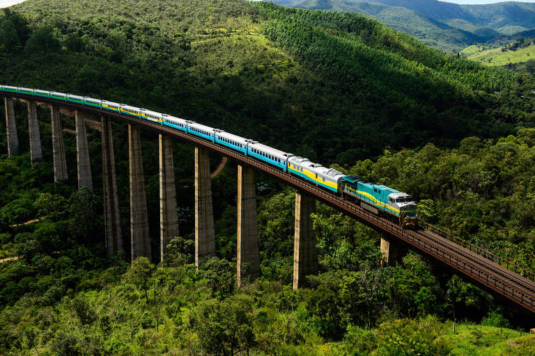 Imagem aérea mostra trem transpondo uma ponte férrea, com vegetação na parte de baixo e ao fundo