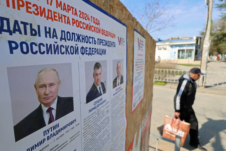 Morador de Evpatoria, na Crimeia anexada, passa por cartaz eleitoral mostrando Putin e seus rivais
