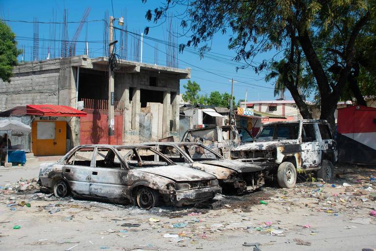 Foto mostra três carros queimados brancos na frente de moradias pobres