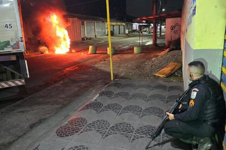 A imagem mostra um policial agachado e uma barricada de fogo
