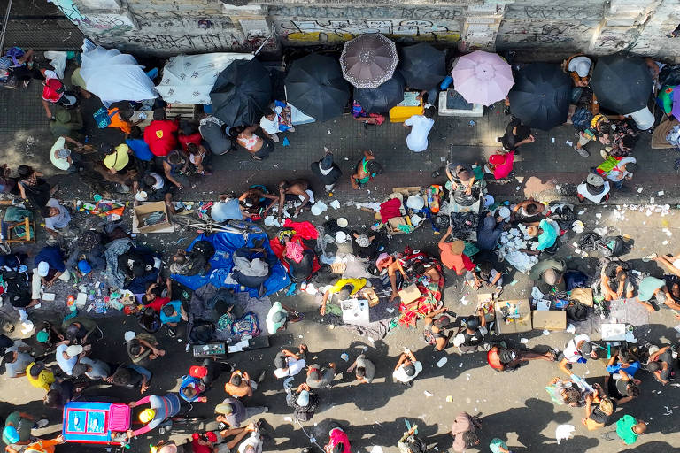 Vista aérea de rua tomada por pessoas, algumas sentadas sob guarda-chuvas e barradas improvisadas com lençóis