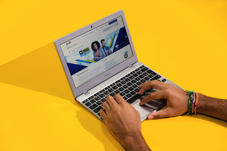Mãos de uma homem digitam em um computador, que está com o programa do Imposto de Renda na tela