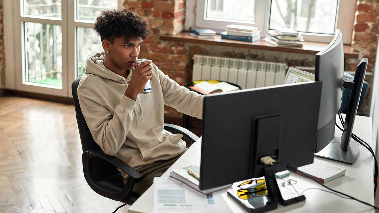 Jovem toma energético em frente ao computador