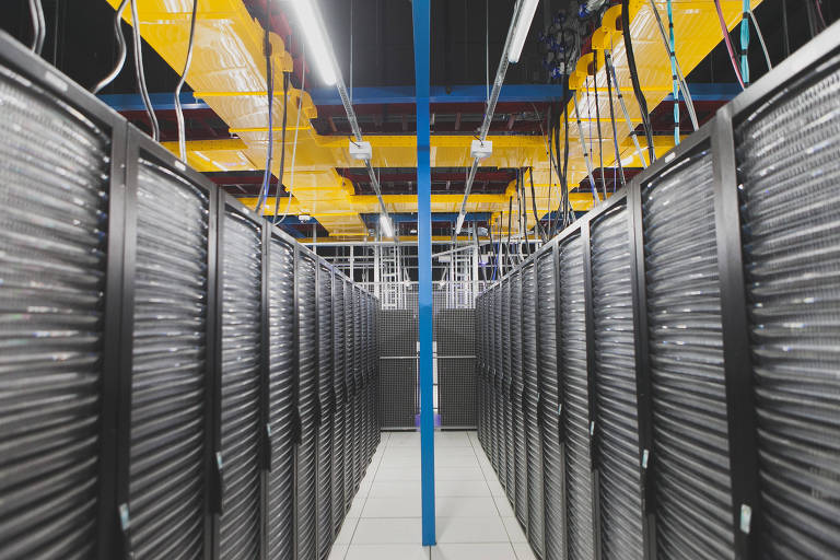 Racks de computadores de data center, cada um deles tem de 20 a 30 servidores. As máquinas são pretas. No telhado, há calhas para passagem de fios amarelas, azuis e vermelhas