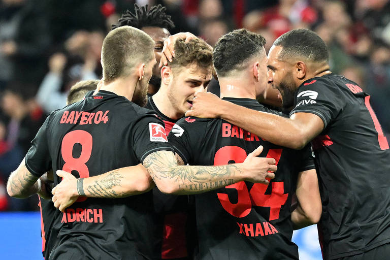 Quatro jogadores do Bayer Leverkusen se abraçam em um círculo para comemorar gol na vitória por 3 a 0 sobre o Bayern de Munique, na BayArena