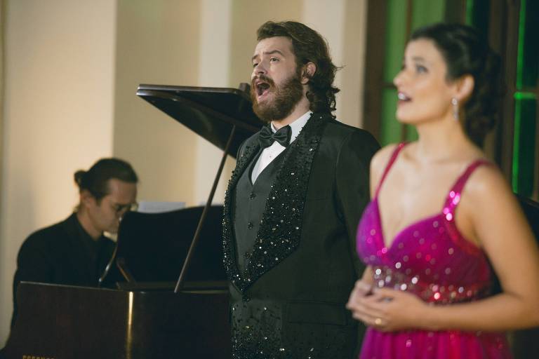 Em foto colorida, cantores de ópera aparecem cantando acompanhados por um pianista