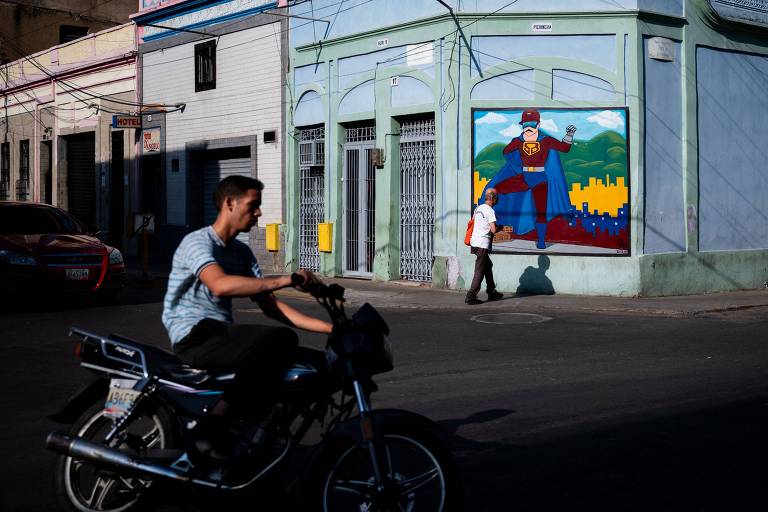 Pessoas caminham perto de mural na capital Caracas estampado com o Super Bigode, o personagem inspirado em Nicolás Maduro e criado pela ditadura como mais uma forma de propaganda