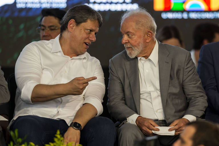 Imagem mostra o governador paulista, um homem de meia idade e cabelos escuros, com camisa de mangas dobradas branca conversando e apontando o dedo para Lula, um homem idoso de cabelo e barba brancas, vestindo camisa branca e pletó cinza