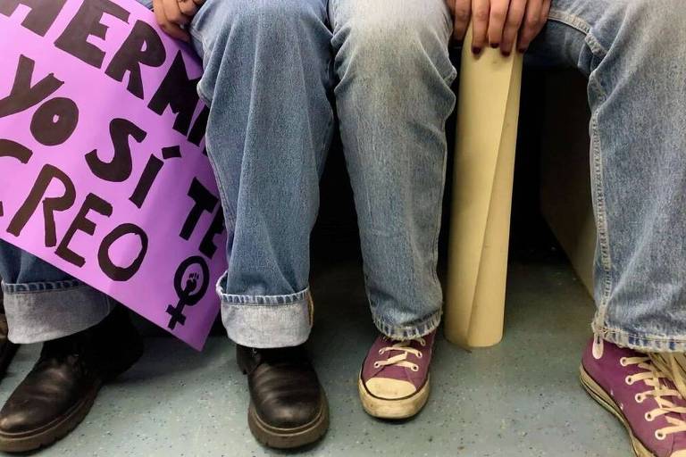 foto mostra pernas de jovens. entre elas, cartazes onde se lê, em espanhol, "irmã, eu, sim, acredito em você"
