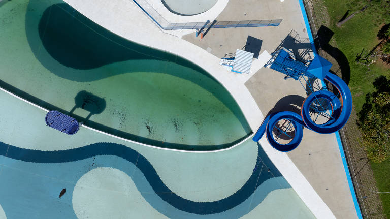 foto aérea mostra detalhes de piscina, com tobogã, água em área esverdeada e outra área, aparentemente mais limpa, da piscina