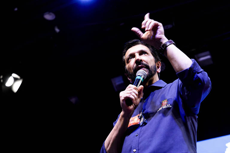 Homem de camisa social azul discursa com microfone na mão