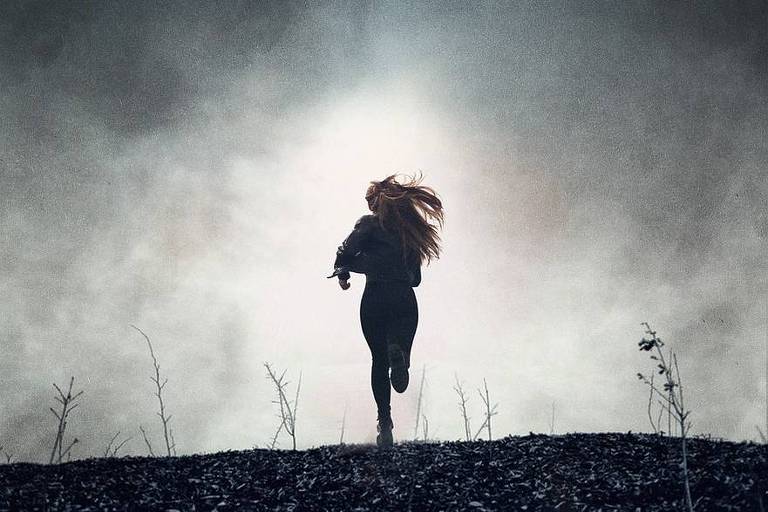 Mulher correndo numa estrada escura, com uma luz no fundo
