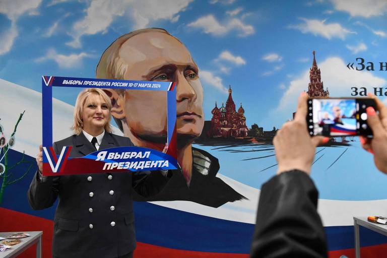 Mulher posa em frente a mural com imagem de Putin após votar, segurando uma moldura para fotografias com os dizeres 'Eu escolhi um presidente', na Donetsk ocupada pela Rússia